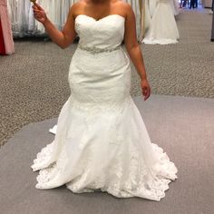 a woman in a white wedding dress is holding up a gold object and posing for the camera