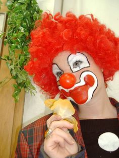 a man with red hair and clown makeup holding a piece of food in his hand