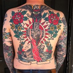 the back of a man with tattoos on his body and arms, holding a cross