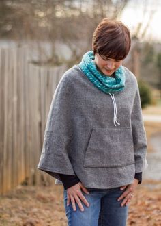 a woman wearing a gray ponchy with a blue scarf around her neck and hands on her hips