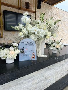 white flowers in vases sitting on top of a stone counter next to a sign