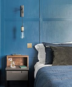 a bedroom with blue walls and a wooden night stand next to the bed in front of it