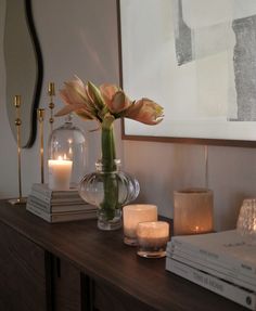 a vase with flowers and candles sitting on a table in front of a framed painting