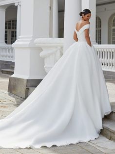 a woman in a white wedding dress standing on some steps with her back to the camera