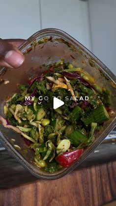 someone is adding ingredients to a salad in a glass dish on a wooden table with the words my go salad