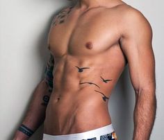 a man with tattoos on his chest standing next to a wall and looking at the camera