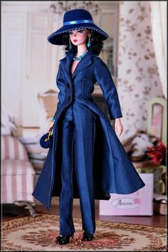 a doll in a blue coat and hat is standing on a rug with a purse