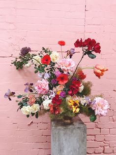 a vase filled with lots of colorful flowers on top of a table next to a brick wall