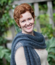 a woman with red hair wearing a blue knitted shawl and smiling at the camera