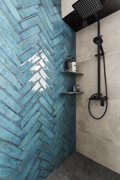 a shower with blue tiles on the wall and shelves in front of it, next to a shower head