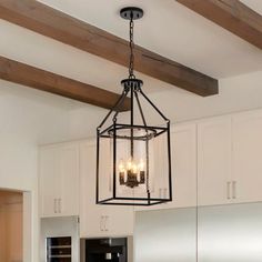 a chandelier hanging from the ceiling in a kitchen with white cabinets and wooden beams