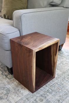 a small wooden table sitting on top of a rug next to a gray couch in a living room