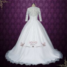 a white wedding dress with long sleeves and lace on the bouncy skirt is displayed in front of a purple background