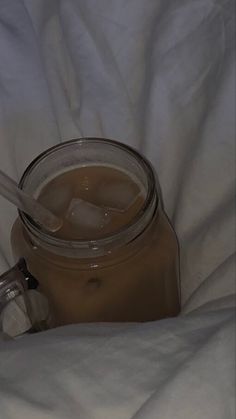 a glass jar filled with liquid sitting on top of a white bed sheet next to a spoon