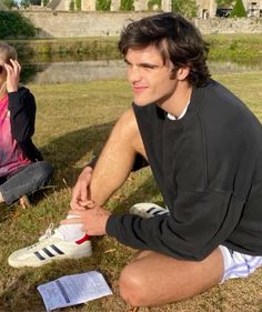 two people sitting in the grass with one person on his cell phone