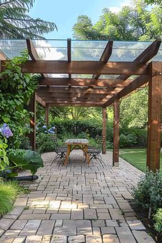 an outdoor dining area with brick walkway and wooden pergoline roof, surrounded by greenery