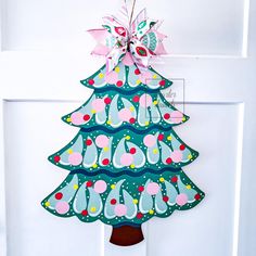 a paper christmas tree hanging on the front door with pink and green ornaments around it