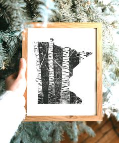 a person holding up a framed print in front of a christmas tree with pine needles