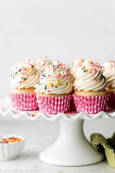 cupcakes with white frosting and sprinkles on a cake stand