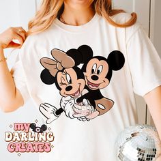 a woman wearing a mickey and minnie mouse t - shirt while holding a disco ball