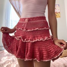 a woman wearing a pink top and red crocheted skirt standing in front of a bed