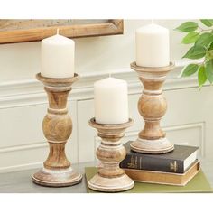 three white candles sitting on top of a wooden table next to a book and potted plant