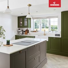 a kitchen with green cabinets and an island in front of a window that has a potted plant on it