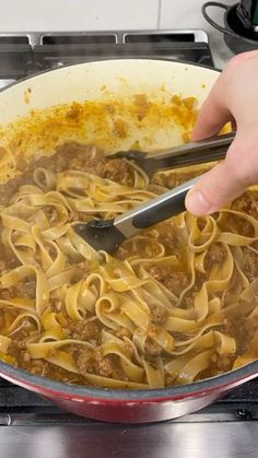 a person is stirring some noodles in a skillet on the stove with tongs