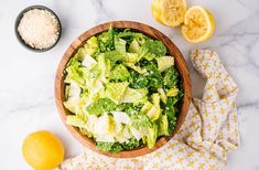 a wooden bowl filled with salad next to two lemons and salt on top of a white counter