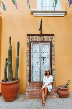 a woman sitting in front of a door next to potted plants and cacti