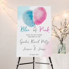 a blue and pink watercolor balloon wedding sign on a easel with lights in the background