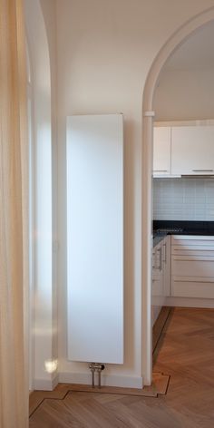 an empty kitchen with white cabinets and wood flooring is seen from the doorway to the living room