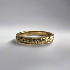 a yellow gold wedding ring with an intricate design on the outside and inside, sitting on a white surface