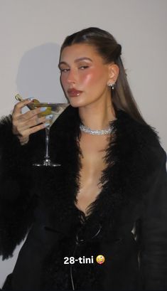 a woman holding a martini glass in her right hand and wearing a black fur coat