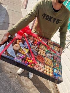 a man is holding a large tray full of food and candy on the street while wearing a t - shirt that says, no manes cuero