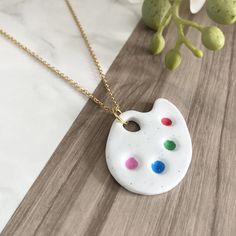 a necklace with a paint palette on it sitting on a table next to some flowers