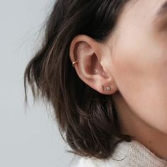 a close up of a person wearing ear piercings and a white turtle neck sweater