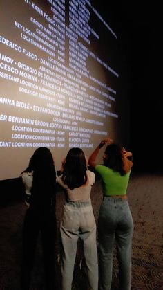 two women standing next to each other in front of a wall with words on it