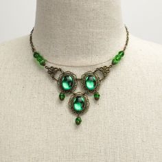 Marquesa Questa jeweled Renaissance necklace in antique bronze metals with emerald green gems Some jewelry was simply made to turn heads. Attract the wandering eye of a nobleman or even a prince with an enticing accessory. Slip on this Marquesa Questa jeweled Renaissance necklace and revel in the stares and praise.This jaw-dropping necklace features three brilliant oval emerald green gems, each mounted in antique bronze. Faceted emerald green crystals capped in the same bronze filigree hang from Green Emerald Cabochon Necklaces, Green Emerald Cabochon Necklace, Green Emerald Jeweled Necklace, Green Emerald Bohemian Necklace, Green Jeweled Emerald Necklace, Antique Jeweled Metal Jewelry, Victorian Style Metal Jewelry With Jewels, Emerald Jeweled Necklaces As Gifts, Emerald Jeweled Necklaces For Gifts