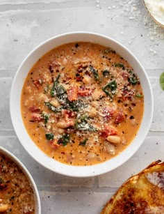 two bowls filled with soup next to bread on a white counter top and one bowl is full of soup