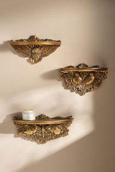 two gold wall mounted shelves with candles on them and one candle holder in the shape of an eagle