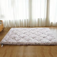 a mattress is on the floor in front of a window with white curtains and wooden floors