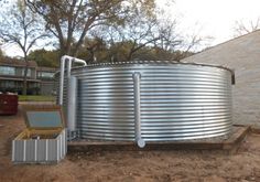 a large metal tank sitting in the middle of a dirt field next to a building