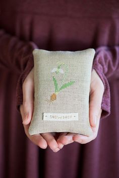 a person holding a pillow with a cross stitch design on it that says, i love flowers