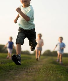 three young children running down a dirt path in the grass, with one child holding a frisbee