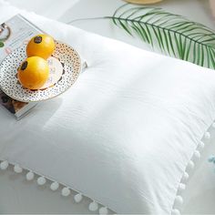 a white pillow with pom - poms on it and some oranges in a bowl