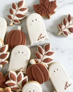 cookies decorated with leaves and ghost faces on a marble countertop, surrounded by fall decorations