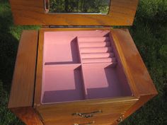 an open wooden box with pink napkins in it on the grass near a tree