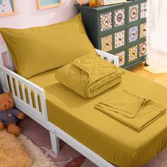 a bed with yellow sheets and pillows in a room next to a teddy bear on the floor