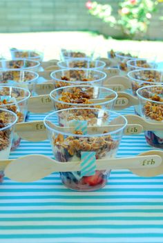 a table topped with plastic cups filled with fruit and granola toppings on top of wooden spoons